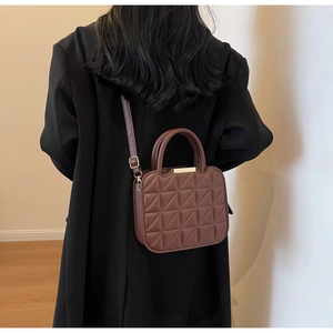 Close-up of a quilted dark brown crossbody bag with metal top handle on a black coat