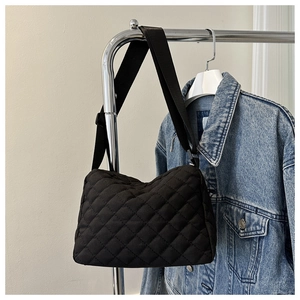 Detail of black quilted shoulder bag with adjustable strap over a denim jacket