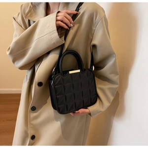 Close-up of black quilted small square bag with gold hardware worn with khaki trench coat