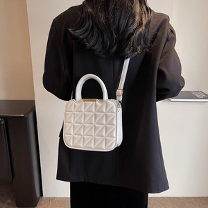 White quilted crossbody bag with top handle and gold accents on a stylish model