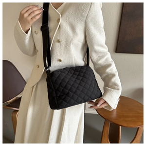 Detail of black quilted shoulder bag featuring adjustable woven strap and diamond patterns
