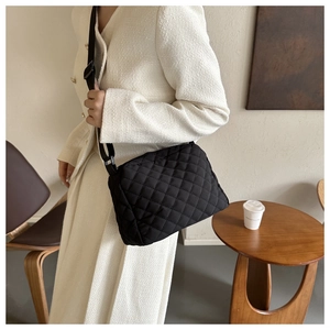 Detail of black quilted crossbody bag with adjustable wide strap on shoulder