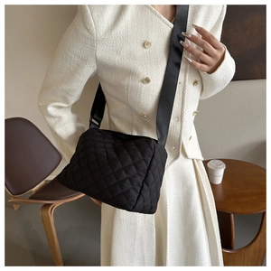 Detail of black quilted crossbody bag with wide nylon strap worn by a model in interior