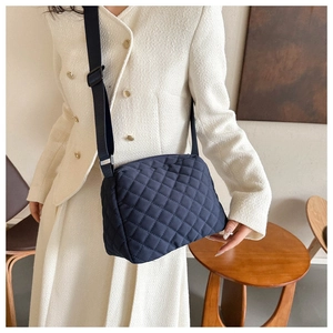 Quilted navy blue crossbody bag with adjustable wide strap shown on a cream coat