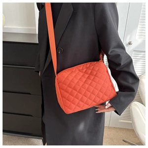 Quilted bright orange nylon shoulder bag with wide strap worn by a model in detail