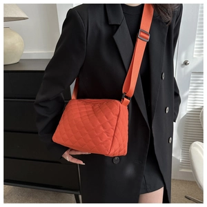 Detail of orange quilted crossbody bag with adjustable wide strap on black blazer