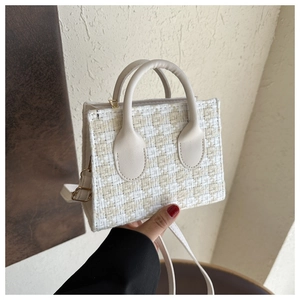 Detail of vintage houndstooth plaid weave texture and white leather handles on handbag