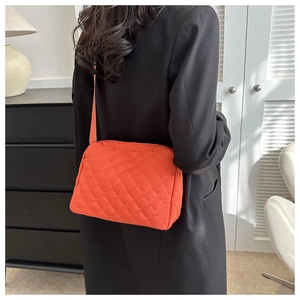 Detail of bright orange quilted nylon crossbody bag showing size on a model's back