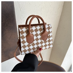 Detail of a brown and white checkered wool crossbody bag with leather handle and strap