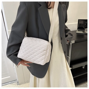 Detailed close-up of white quilted crossbody bag with adjustable wide fabric shoulder strap