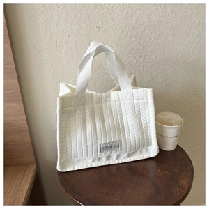 Detail of white quilted tote bag featuring vertical stitching and a Fashion Bag fabric label