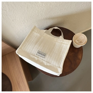 Close-up of cream quilted tote bag with vertical pleats and Fashion Bag woven label