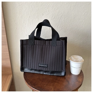 Close-up of black quilted tote bag with vertical stripes and Fashion Bag label on a table
