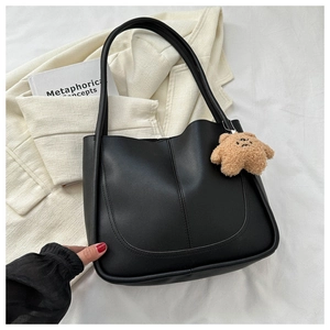Detail of a black PU leather tote bag with curved stitching and a brown teddy bear charm