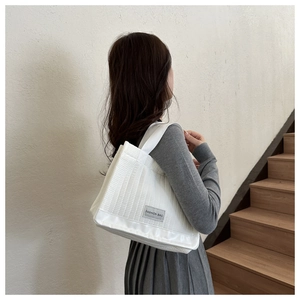 Detailed view of quilted white tote bag with vertical stitching and fashion label