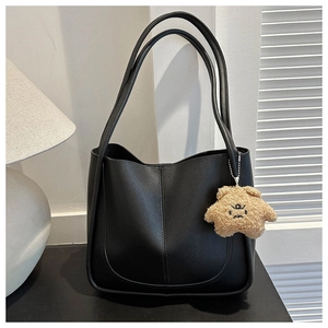 Detail of black faux leather tote bag with a cute plush charm in minimalist interior