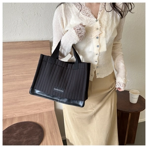 Detail of a black quilted tote bag with longitudinal stitching and fashion textile label