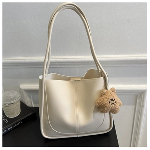 Detail of minimalist cream PU tote bag featuring a cute brown fuzzy bear charm attachment