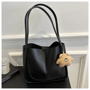 Detail of a black matte PU leather tote bag featuring a cute brown plush bear charm