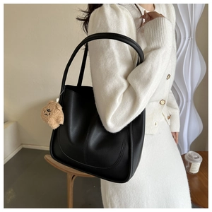 Detail of black matte PU leather tote bag with a cute light brown plush bear charm