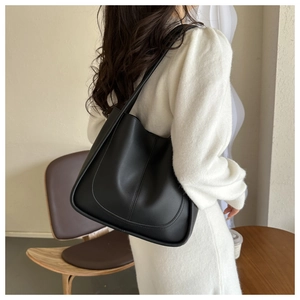Detail of minimalist black PU leather tote bag with curved stitching on a model