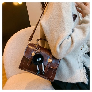 Détail d'un sac à bandoulière vintage marron foncé avec boucles et pompon sur un mannequin