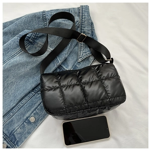 Détail de sac bandoulière en nylon matelassé noir avec boucle dorée sur fond denim