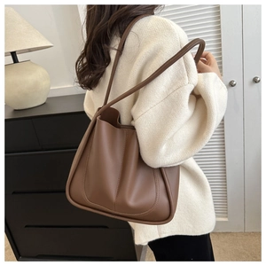 Detail view of coffee brown PU leather tote bag worn as a shoulder bag on a female model