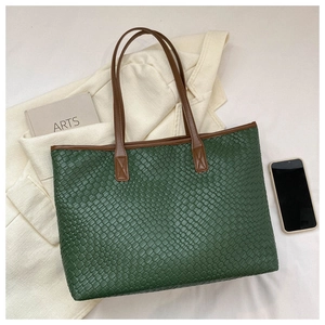 Détail du cabas tissé vert foncé avec anses marron sur un bureau minimaliste