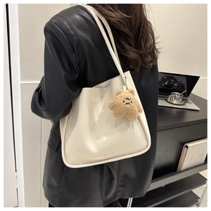 Detail of a creamy white PU leather tote bag with a cute brown plush bear charm