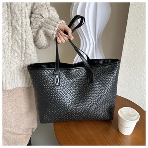 Détail d'un grand sac cabas noir tressé avec de longues anses dans un décor quotidien