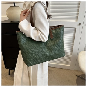 Détail du sac cabas vert foncé tissé avec anses en cuir marron porté à l'épaule