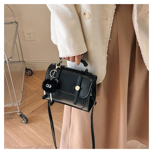 Détail d'un petit sac bandoulière noir vintage avec pompon porté par un mannequin