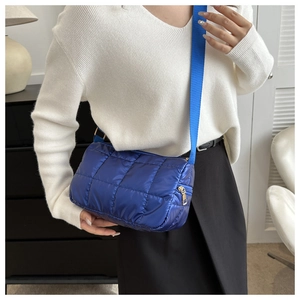 Detail of royal blue quilted shoulder bag with golden zipper and woven strap