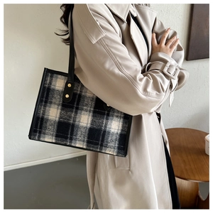 Detail of wool plaid tote bag with black leather handles and gold rivet accents