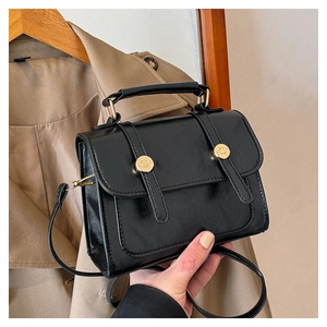 Dettaglio borsa nera in pelle PU con fibbie dorate su un trench beige elegante