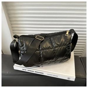Detail of black quilted puffer crossbody bag with adjustable strap and golden zipper on white books
