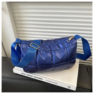 Close-up of vibrant royal blue quilted shoulder bag with wide nylon strap on white books