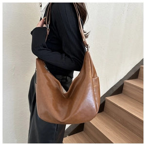 Large caramel brown faux leather tote bag worn on shoulder by model against a white wall