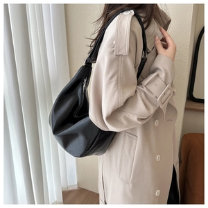 Woman wearing a black faux leather hobo shoulder bag over a beige trench coat