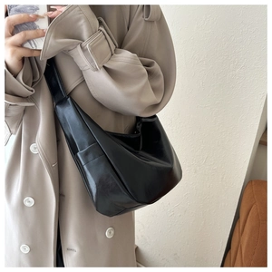 Minimalist black matte leather underarm bag shown on model wearing a beige trench coat
