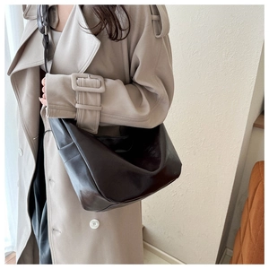 Detail of dark brown glossy leather Hobo shoulder bag worn with a beige trench coat