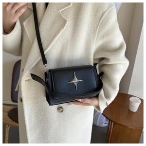 Dettaglio borsa a tracolla in pelle nera con stella d'argento su cappotto beige