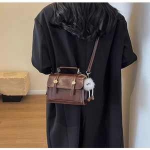 Dark brown retro messenger bag with metal handle and white plush charm on model