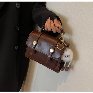 Detail van donkerbruine vintage tas met gouden gespen en een witte pluche hanger