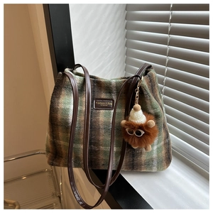 Detail of wool bucket bag featuring green plaid pattern and cute monster plush charm