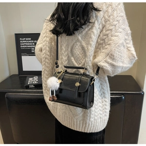 Black vintage messenger bag with metal buckles and white pompom charm in lifestyle setting