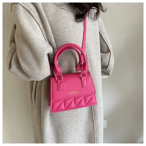 Detailed view of rose pink crossbody bag with quilted diamond pattern on oatmeal coat
