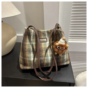 Close-up of wool plaid tote bag with brown leather handles and a cute lion plush charm