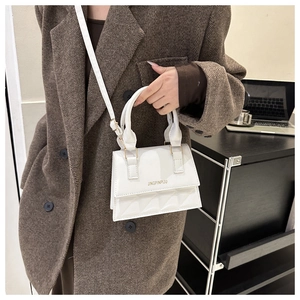 Detail view of a white quilted crossbody bag with gold logo on a professional model